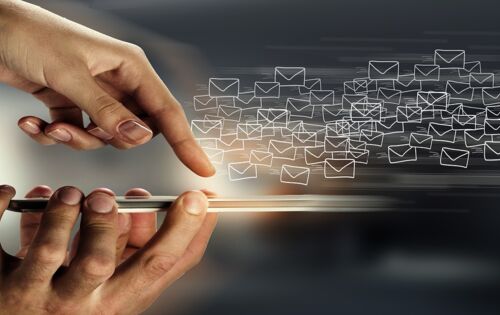 Eine Hand hält ein Smartphone, eine andere tippt auf das Display. Zahllose E-Mail-Symbole fliegen heraus.