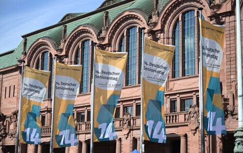 Mehrere Fahnen mit der Aufschrift „14. Deutscher Seniorentag – Worauf es ankommt“ wehen vor der Fassade des Congress Centers Rosengarten in Mannheim. Die Veranstaltung fand vom 2. bis 4. April 2025 statt.